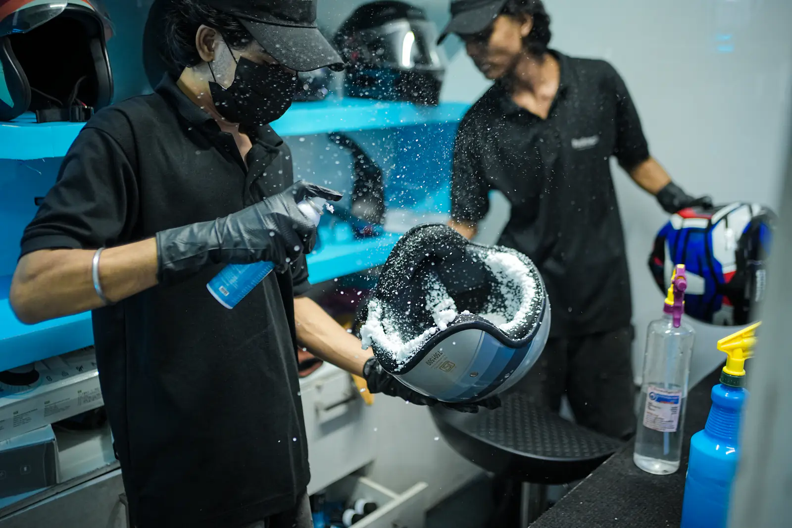 Two technicians deep-cleaning helmet liners with foam in the Helmate bay